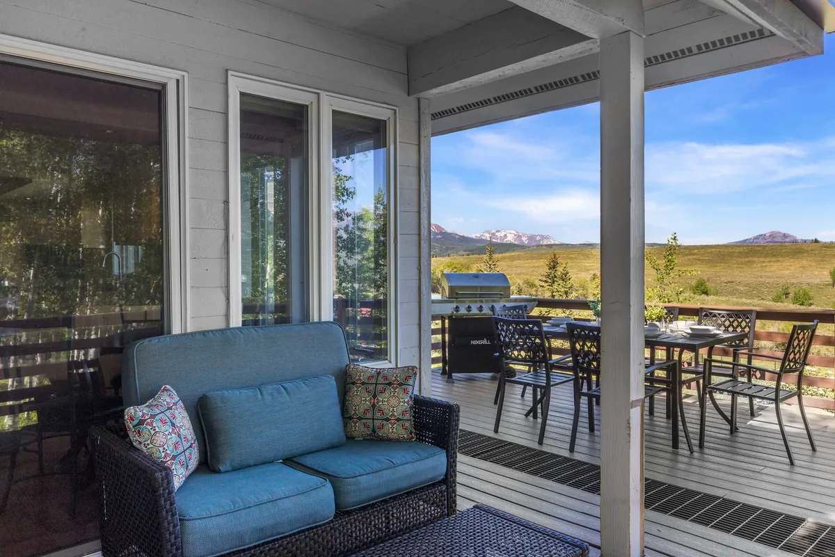 An exterior seating area featuring a comfortable blue sofa and a dining table, all set against a backdrop of majestic mountain views. The space is perfect for relaxing or socializing while immersed in nature.