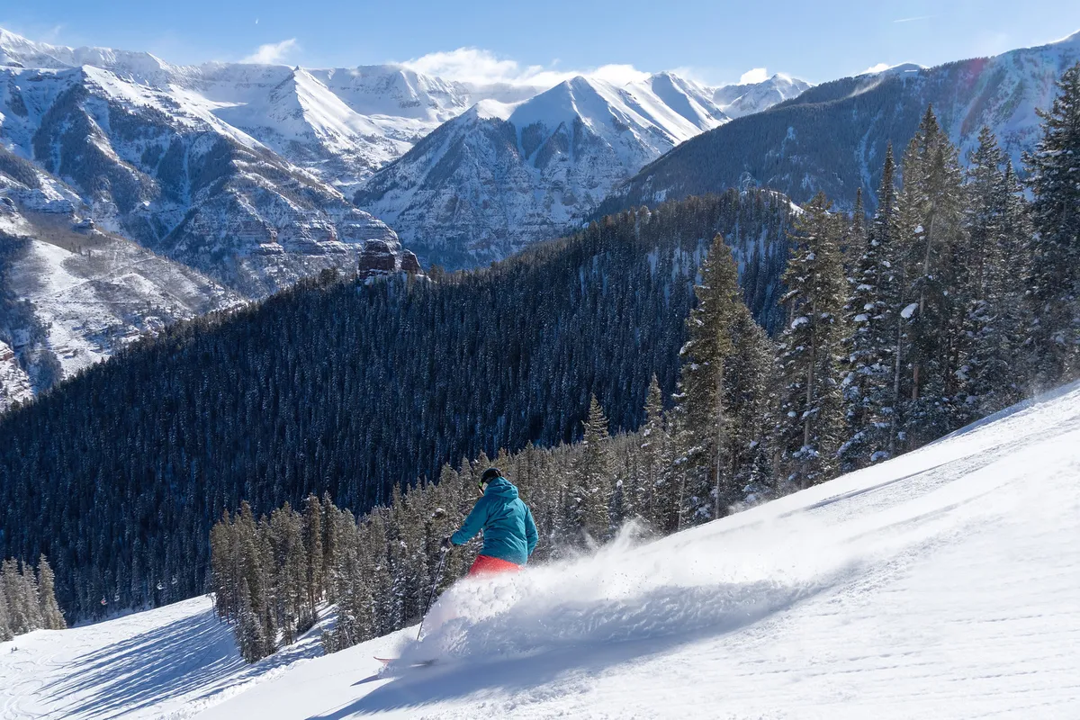 This image features a skier gliding down pristine, snow-covered mountains with evergreen trees dotting the landscape. The action and excitement of winter sports are palpable, and the backdrop hints at the beauty and scale of the nearby slopes.