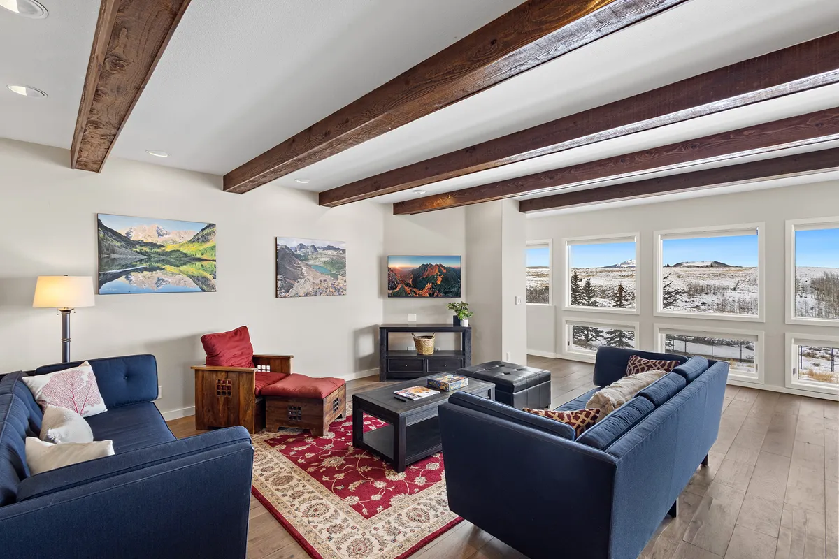 The image showcases a spacious and cozy living room with plush, comfortable sofas arranged for conversation, complemented by tasteful artwork on the walls. Large windows frame stunning mountain views, filling the space with natural light and offering a direct connection to the breathtaking Colorado landscape.