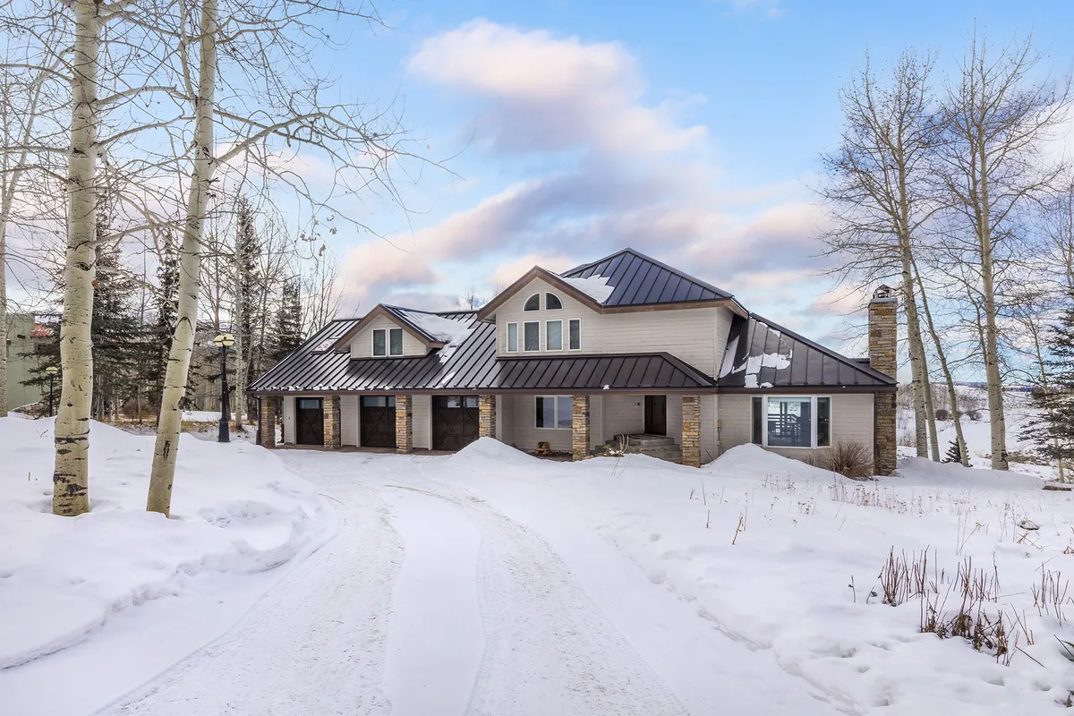 A snow-covered driveway leads to a modern home nestled among aspen trees, with the entire scene blanketed in fresh snow. The peaceful ambiance and architectural style convey both privacy and the magic of a winter wonderland setting.
